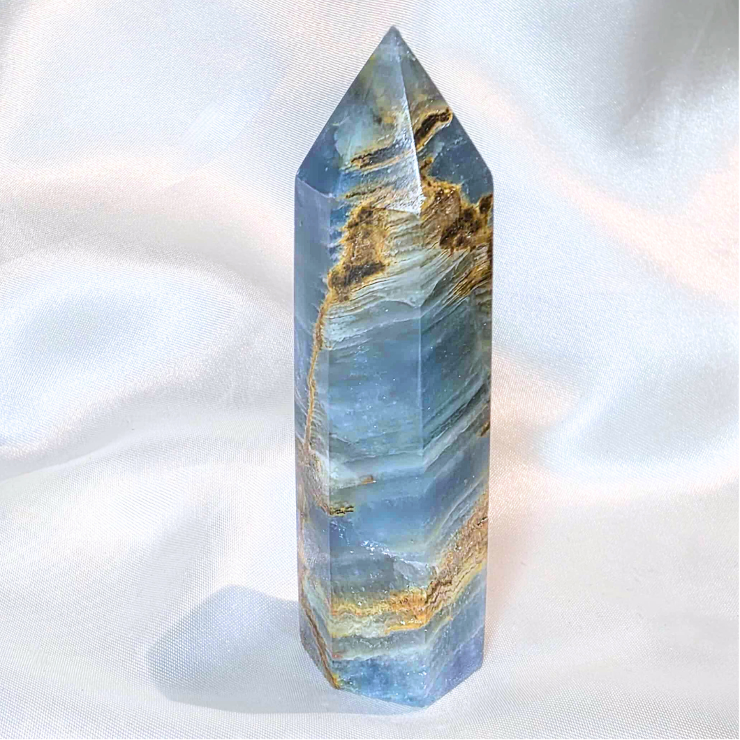 aquatine lemurian Crystal tower with blue and gold patterns on a white fabric background