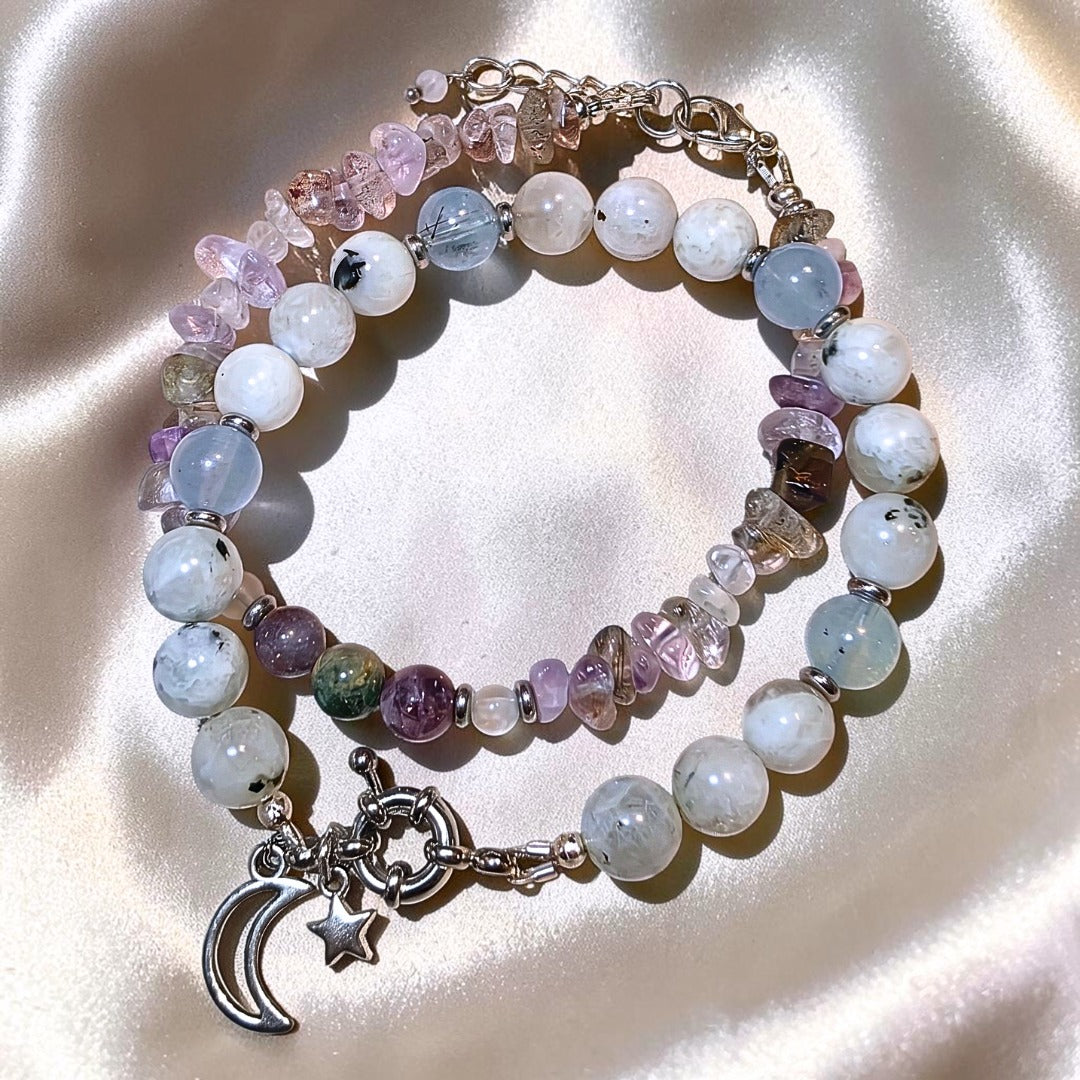 Moonstone bracelet layered with mixed gemstone chip bracelet and silver moon and star charm on champagne satin background