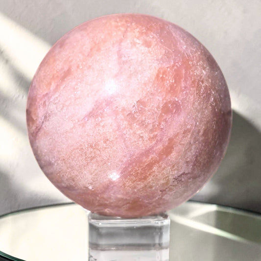 Close up view of a polished pink opal display sphere with natural matrix lines and smooth reflective finish.