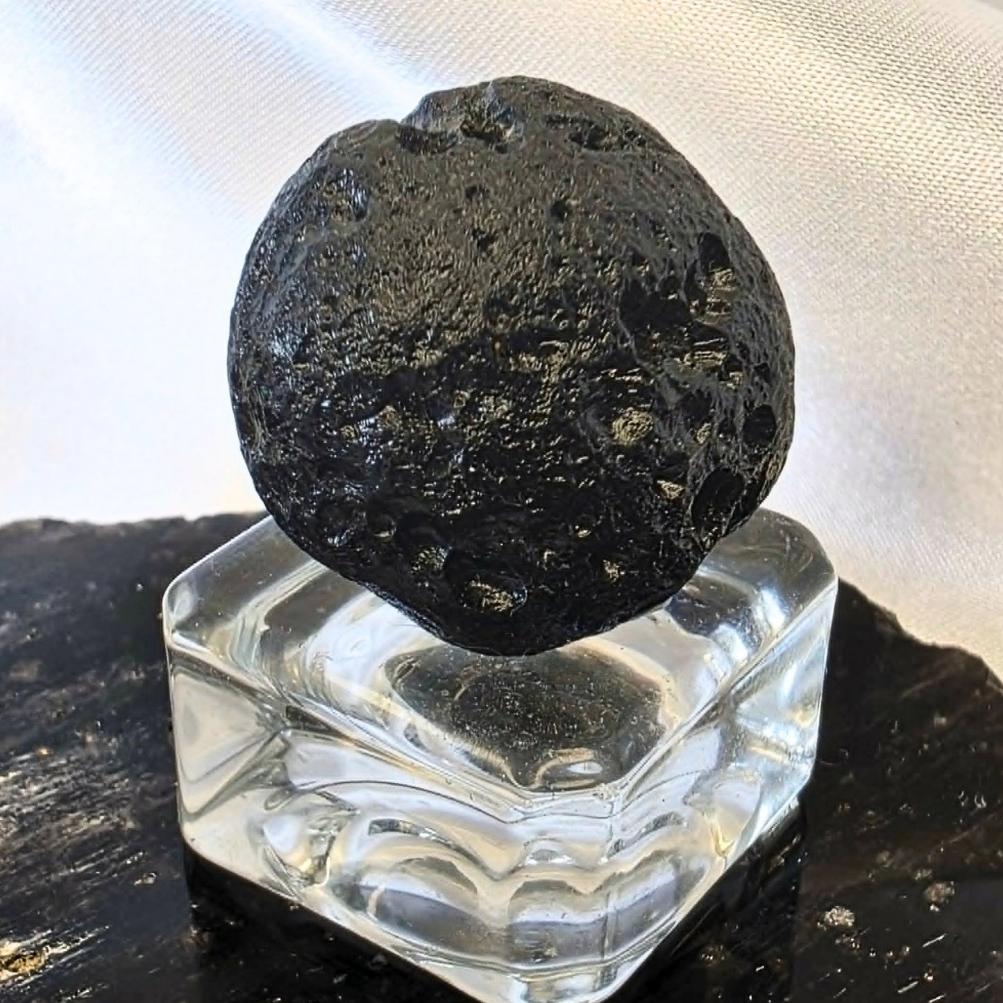 Natural black tektite indochinite impact glass specimen with pitted surface on display stand