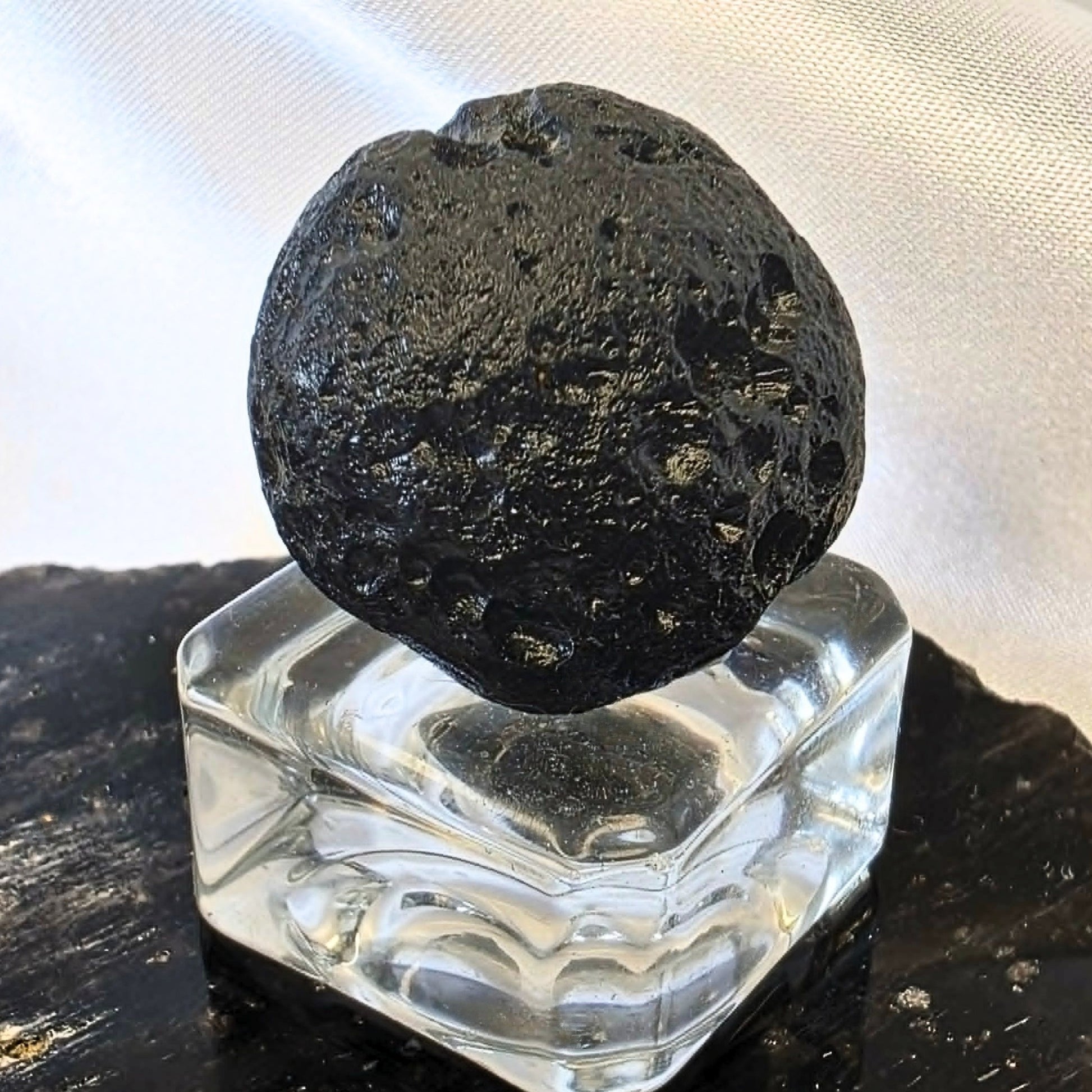 Natural black tektite indochinite impact glass specimen with pitted surface on display stand