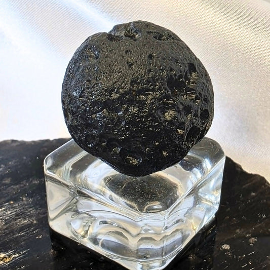 Natural black tektite indochinite impact glass specimen with pitted surface on display stand