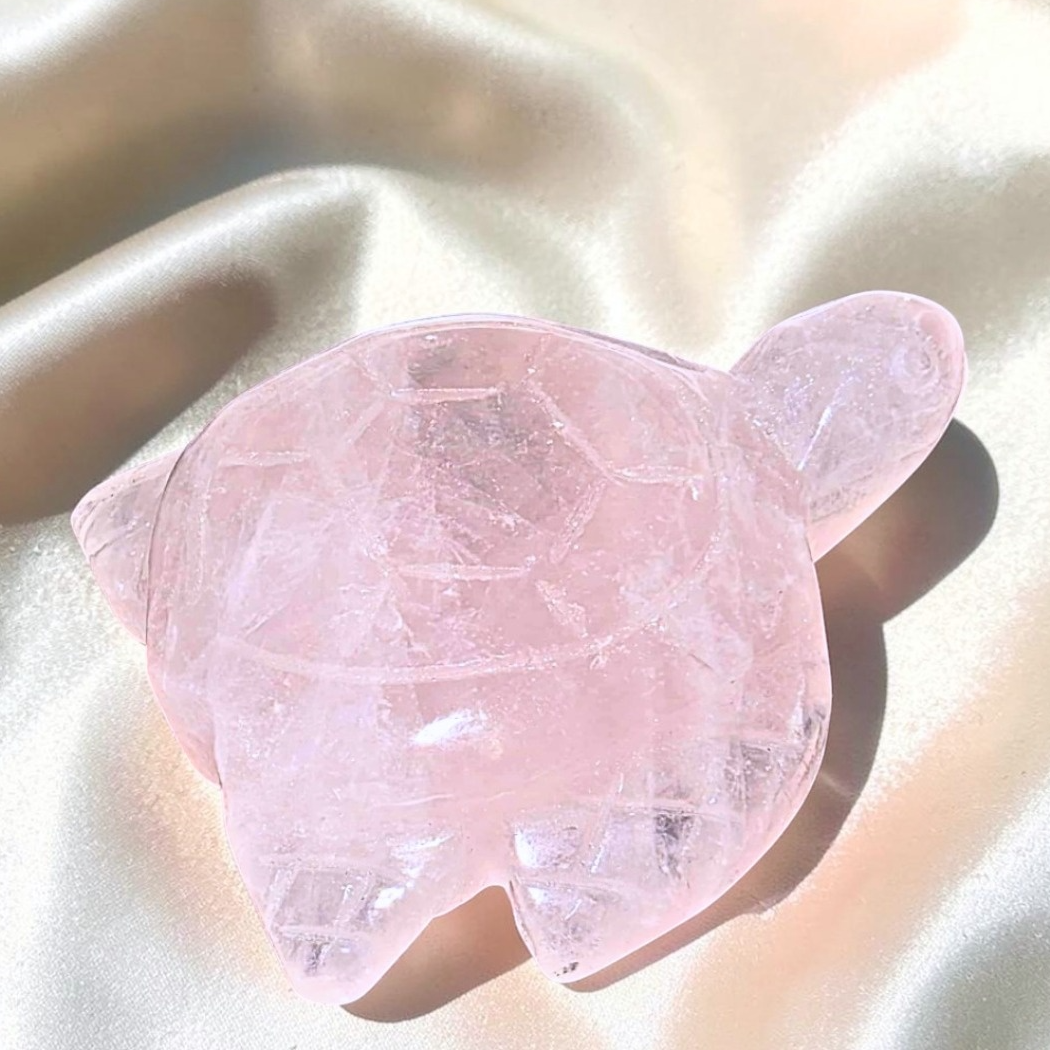 Pink rose quartz turtle carving with small internal rainbows photographed on champagne satin