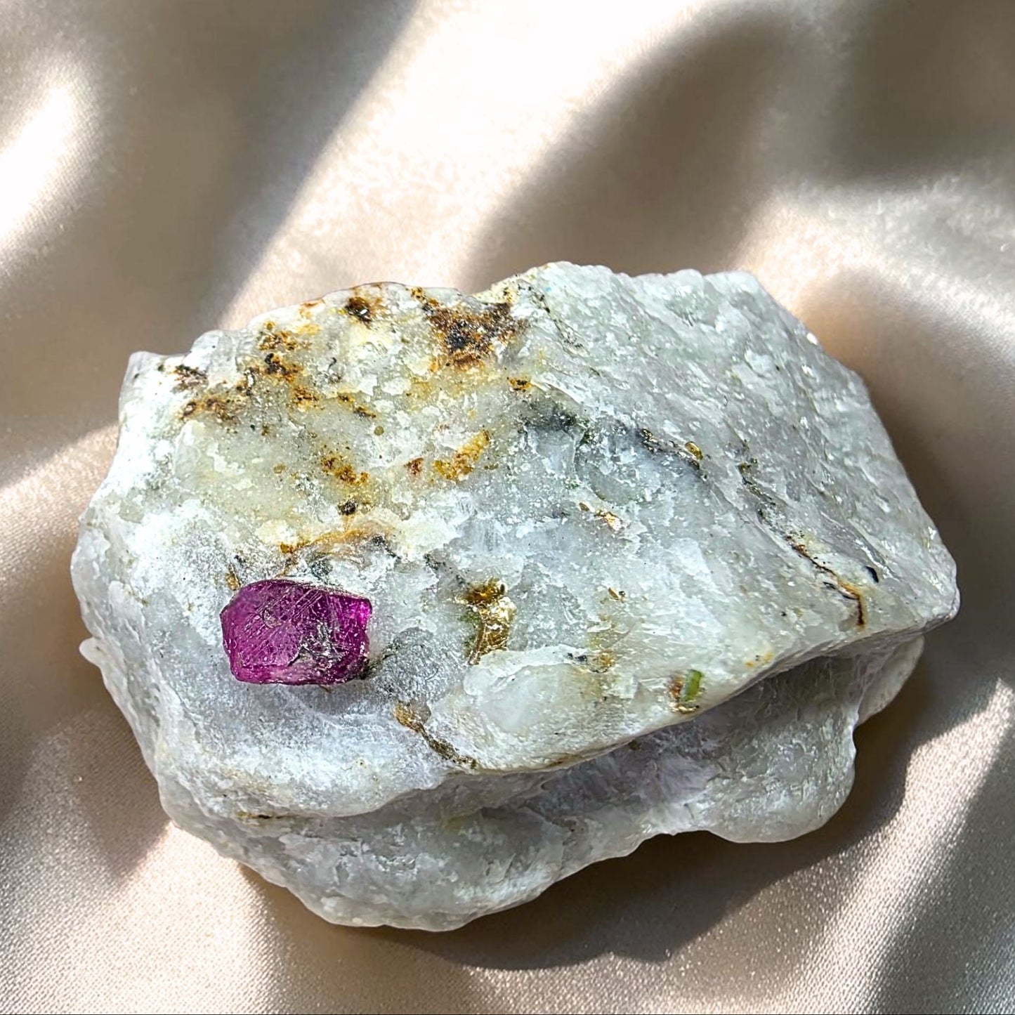 Raw ruby in marble specimen held in hand, showing a bright magenta ruby crystal and small golden pyrite flecks on a white matrix.