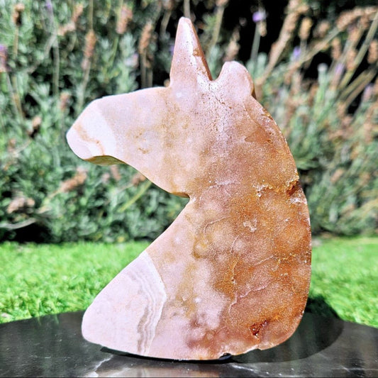 A large Pink Amethyst unicorn carving with various shades of pink and orange from iron inclusions and sparkling druzy Quartz crystals 