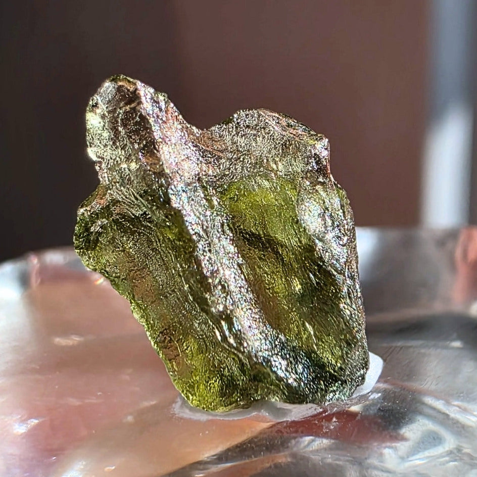 Moldavite crystal on a reflective surface with a blurred background