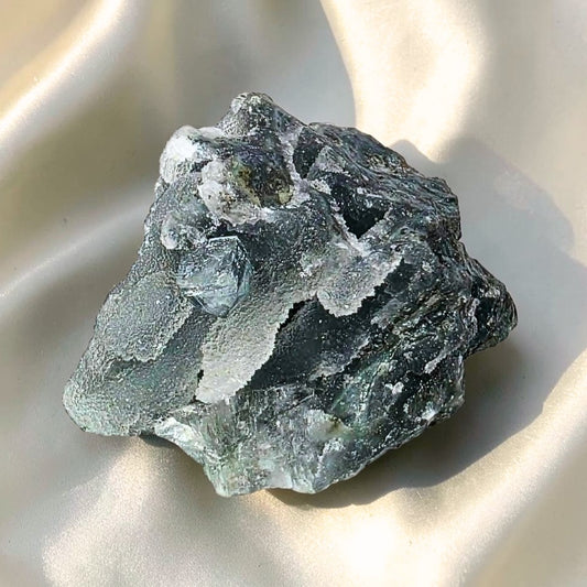 Natural black stalactitic chalcedony specimen with transparent cube-like apophyllite crystals on a champagne satin background.