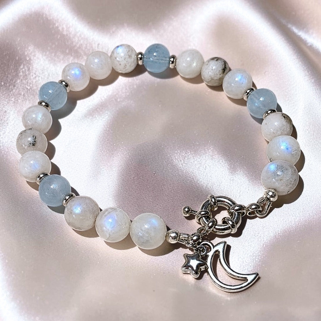 Moonstone and Aquamarine gemstone bracelet with silver moon and star charm on champagne satin background